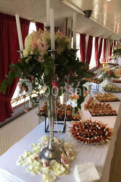 Buffet décoré avec chandeliers, fleurs et pétales, proposant des amuse-bouches variés sur une table blanche.