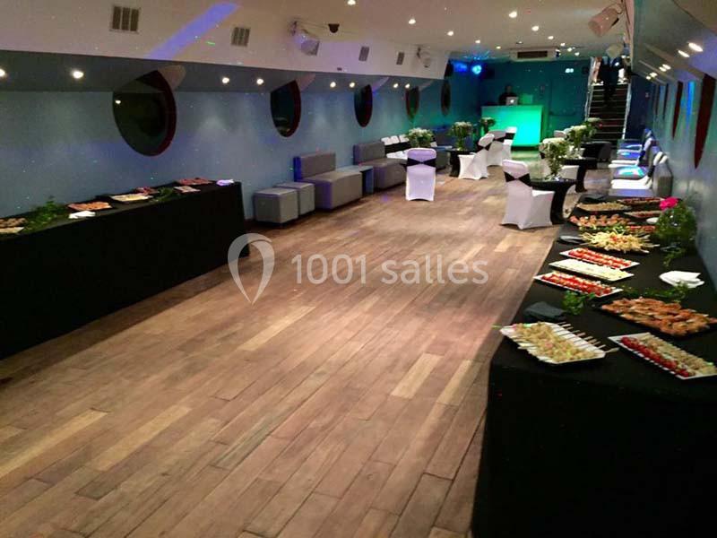 Salle aménagée pour un événement avec tables de buffet garnies, éclairage tamisé et décor moderne.