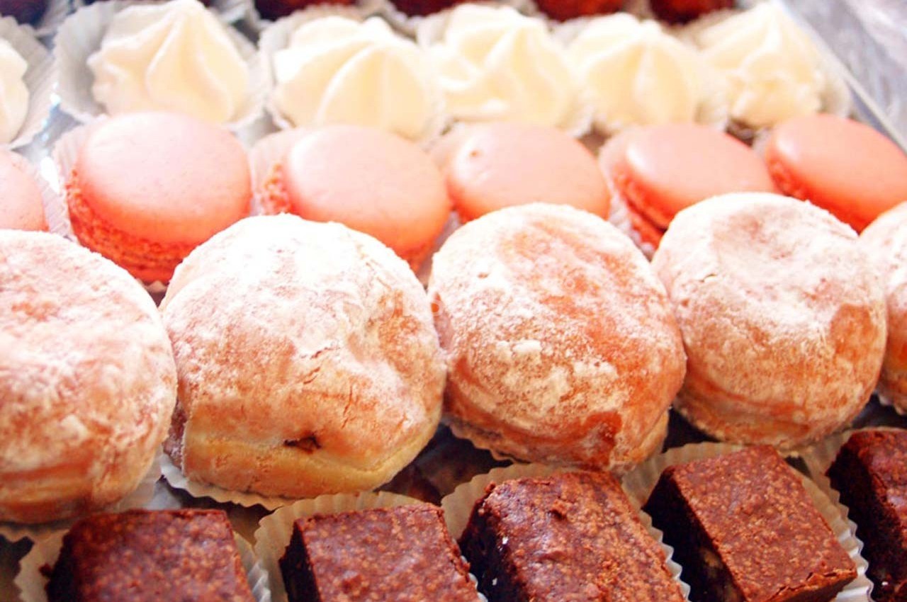 Assortiment de pâtisseries comprenant des macarons roses, des beignets saupoudrés de sucre et des carrés chocolatés.