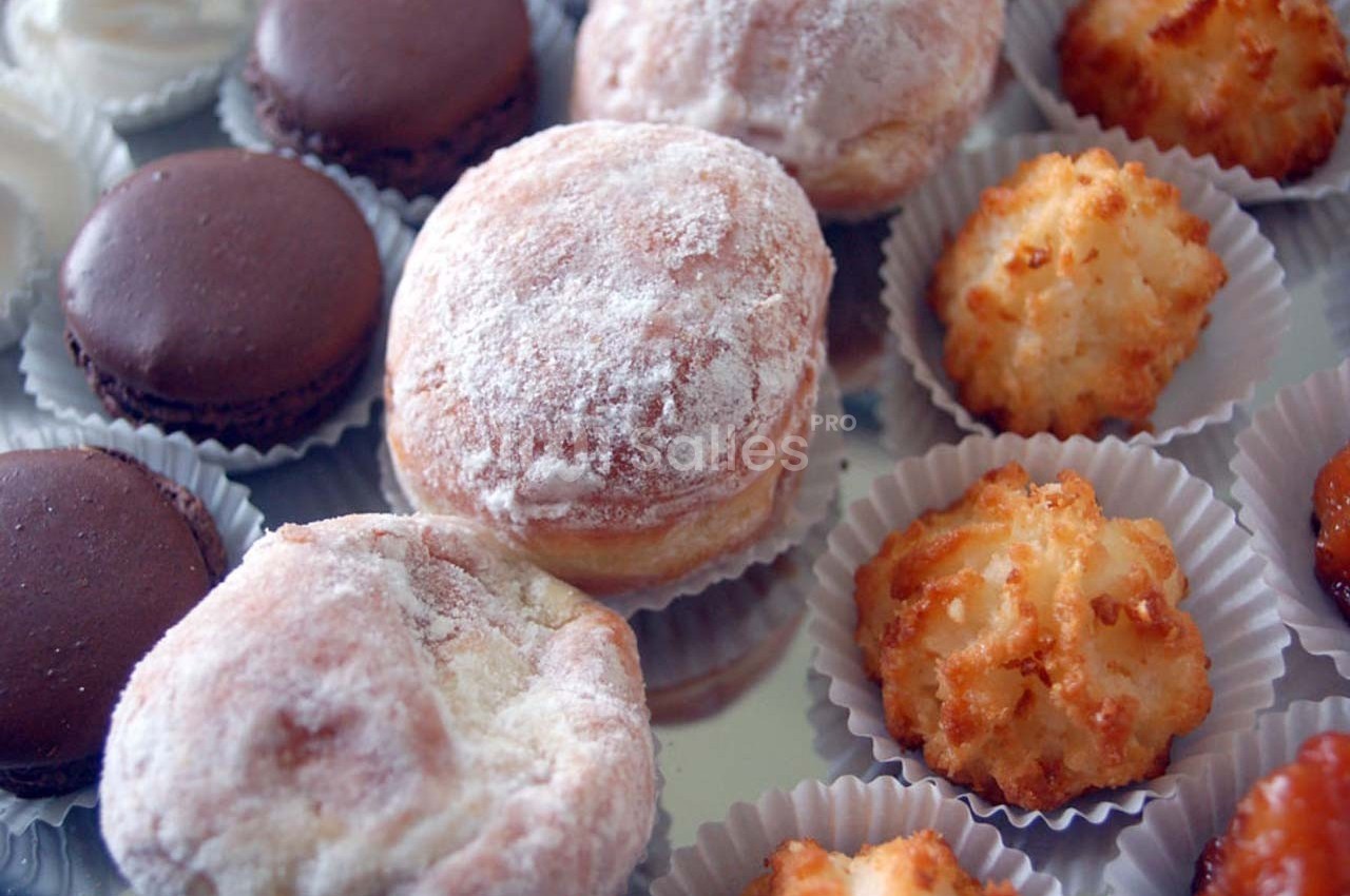 Assortiment de pâtisseries comprenant macarons, beignets saupoudrés de sucre et rochers à la noix de coco.