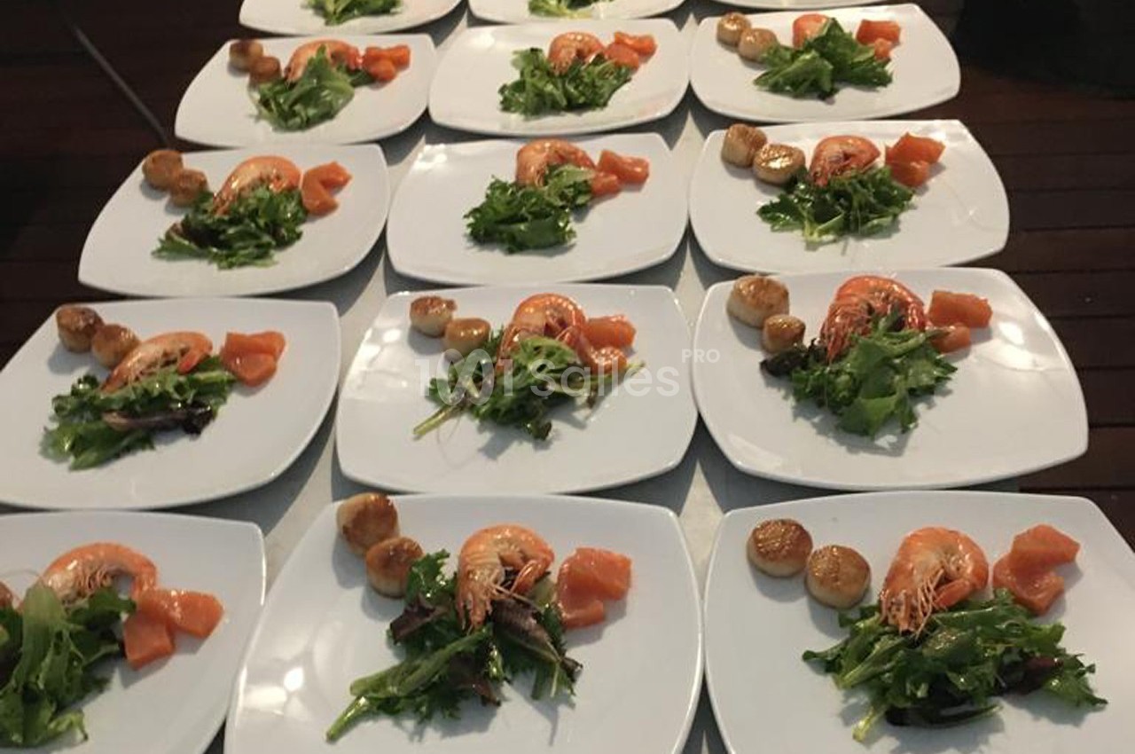 Assiettes dressées avec crevettes, noix de Saint-Jacques, saumon fumé et salade verte sur une table en bois.