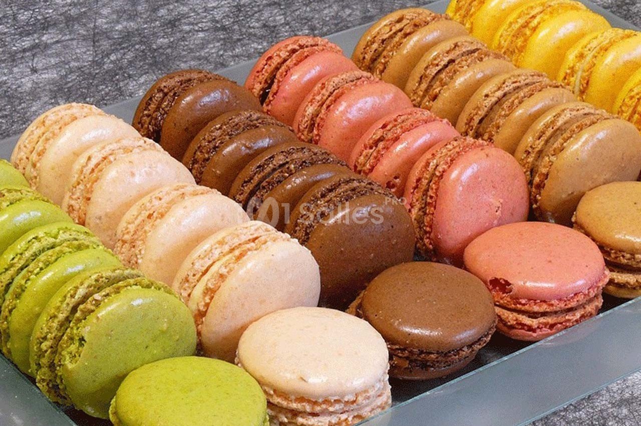 Plateau de macarons colorés alignés en rangées sur une surface grise.