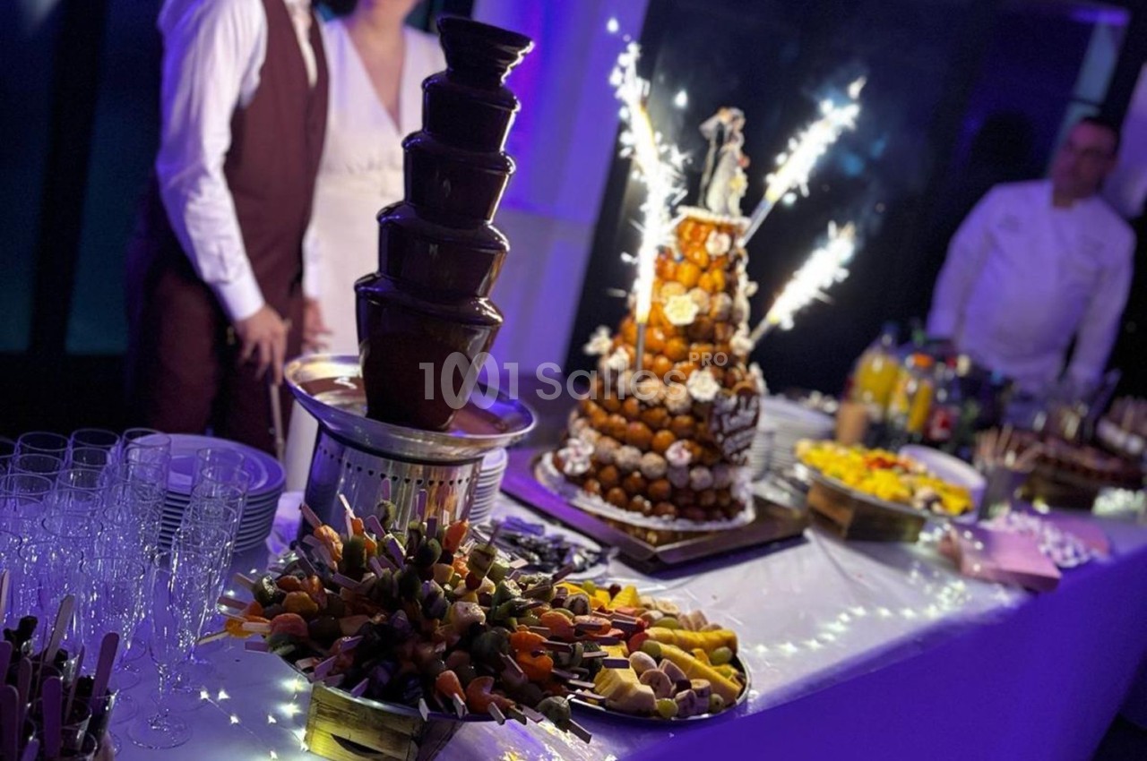 Buffet de desserts avec fontaine de chocolat, pièce montée éclairée de cierges et fruits frais sur une table décorée.