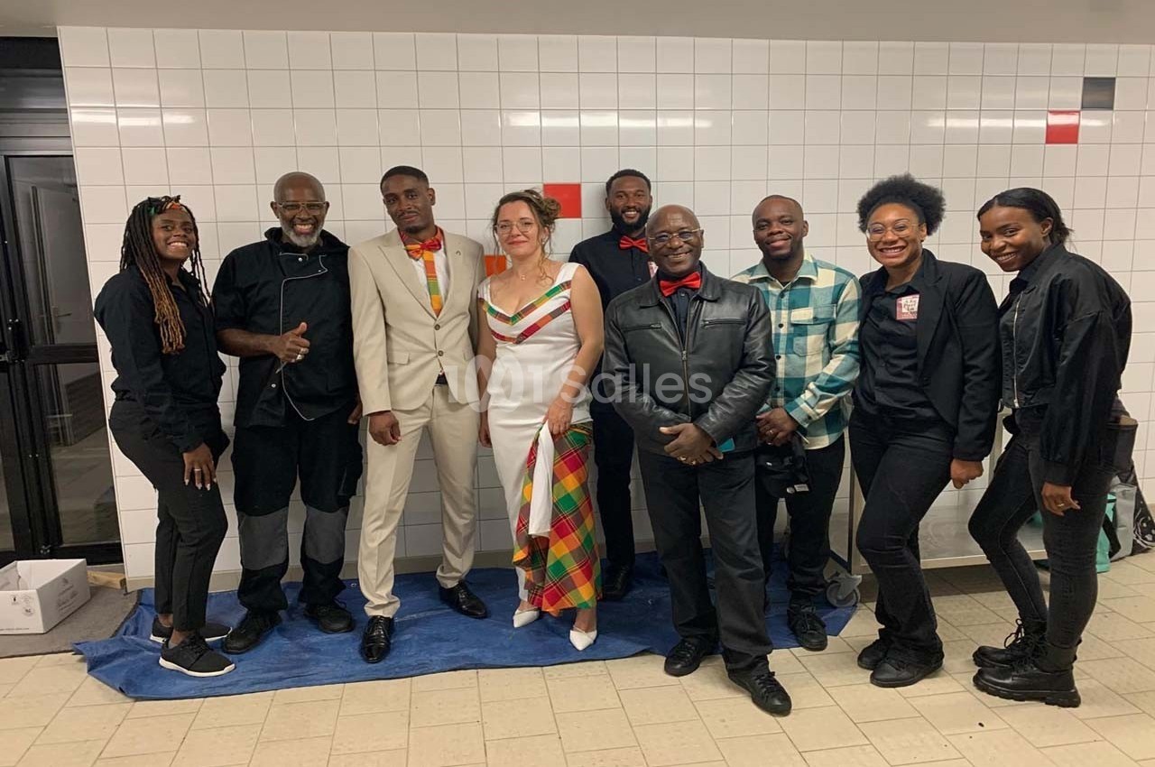 Un groupe de personnes posant ensemble dans un couloir carrelé, certaines en tenue élégante et colorée.