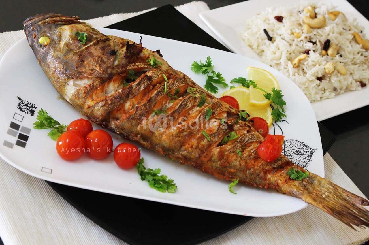 Poisson entier grillé servi avec tomates cerises, rondelles de citron et riz aux noix sur une table.