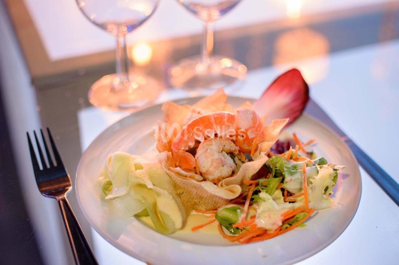Assiette de crevettes avec légumes croquants, chips et sauce, servie sur une table élégamment dressée.