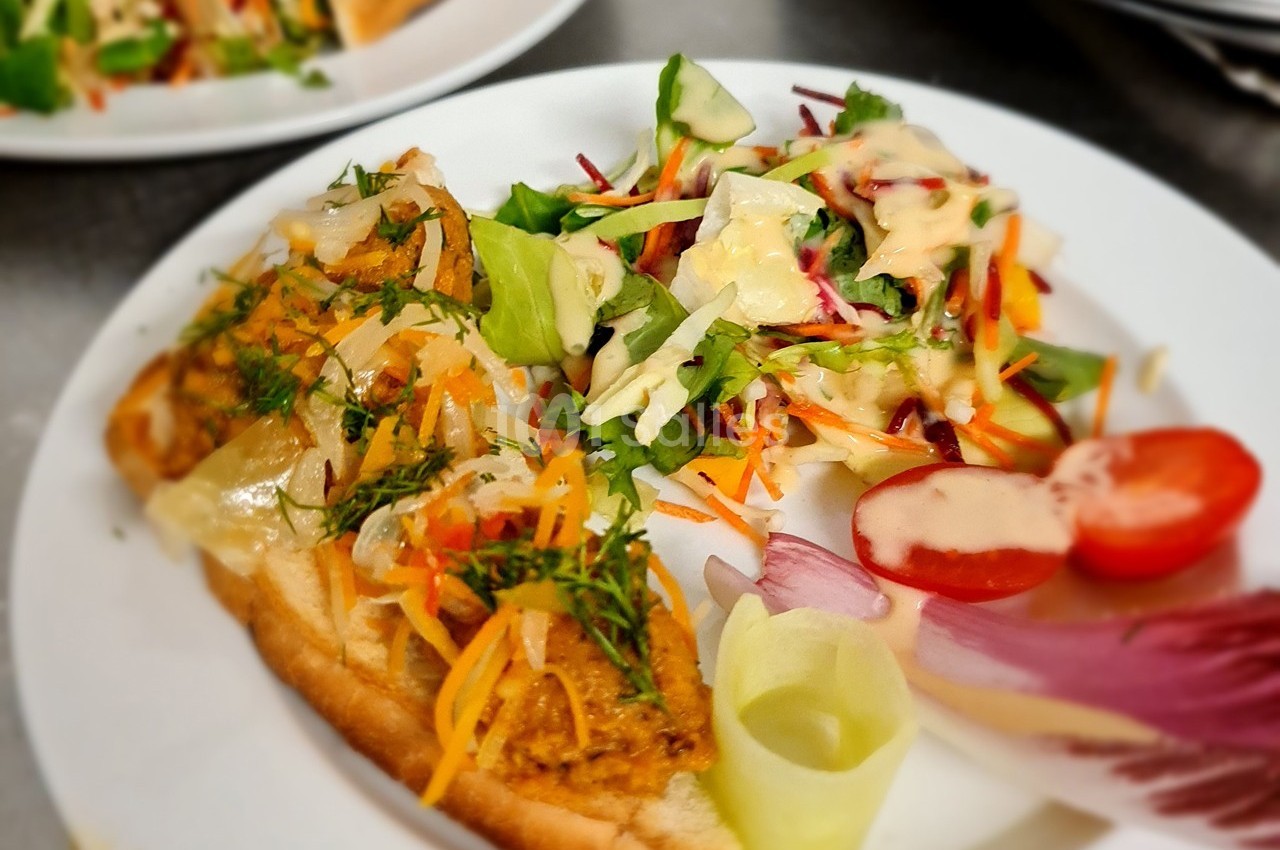 Assiette composée d'une tartine garnie de légumes et d'herbes fraîches, accompagnée d'une salade colorée.