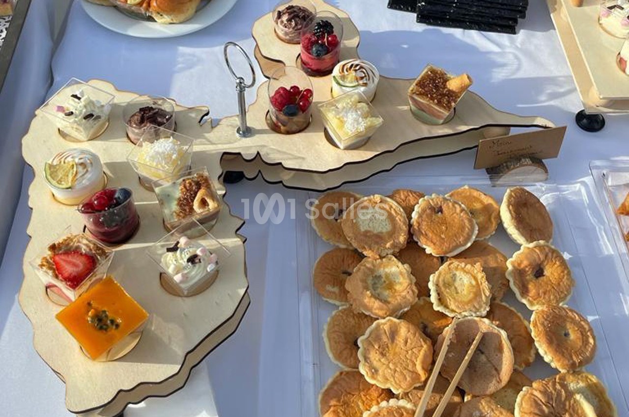 Plateau en bois avec des verrines sucrées variées et des tartelettes disposées sur une table blanche.