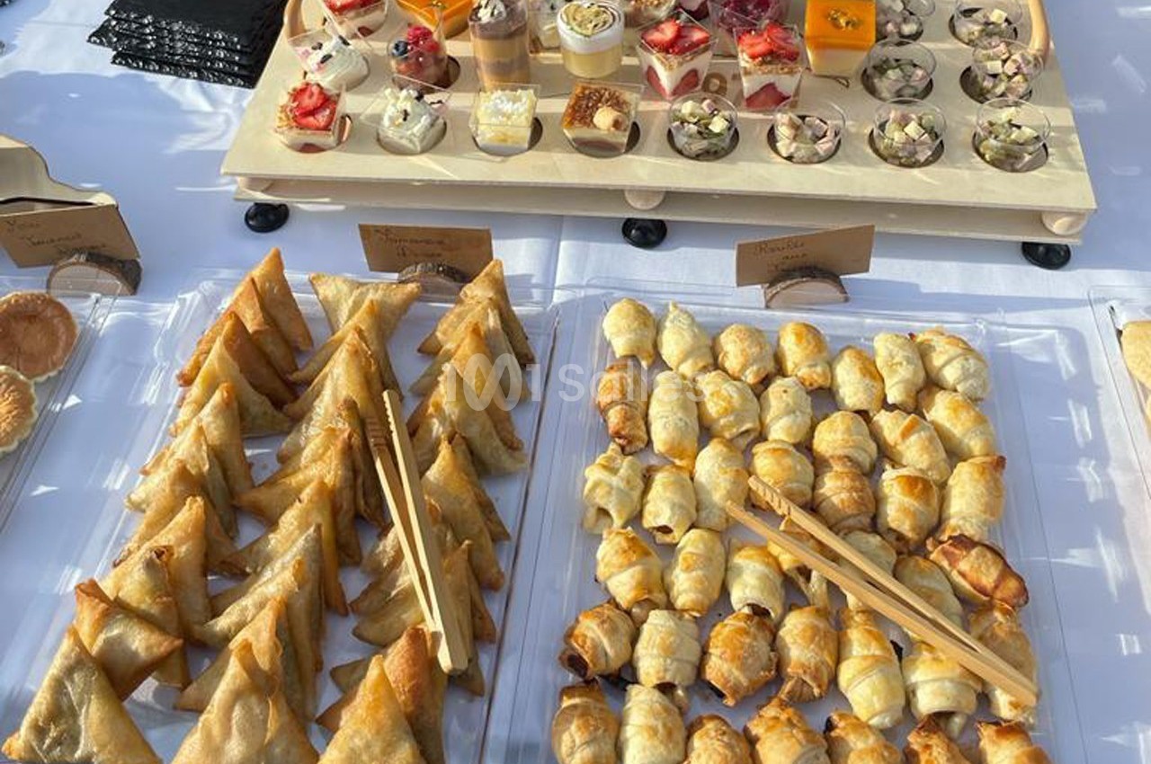 Plateaux de mini-samoussas, feuilletés et verrines sucrées et salées disposés sur une table blanche.