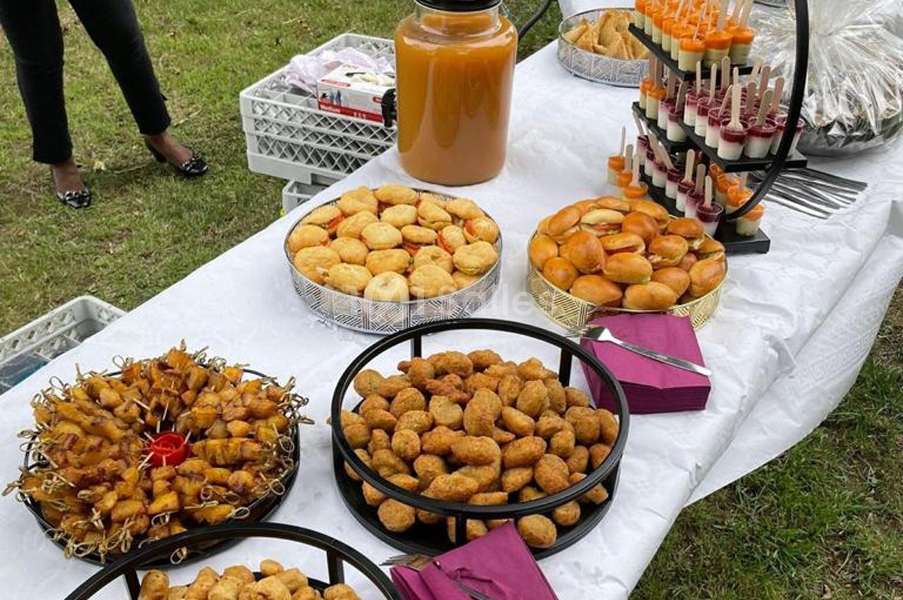 Buffet en plein air avec assortiments de bouchées salées, jus dans un grand bocal et verrines sur un présentoir.