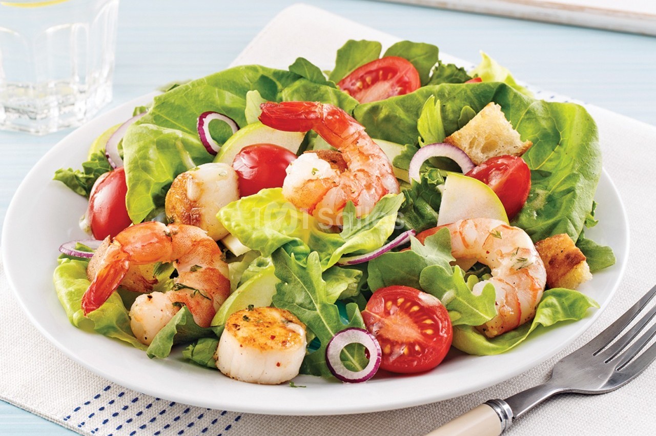 Assiette de salade composée avec crevettes, pétoncles, tomates cerises, oignons rouges, croûtons et feuilles de laitue.