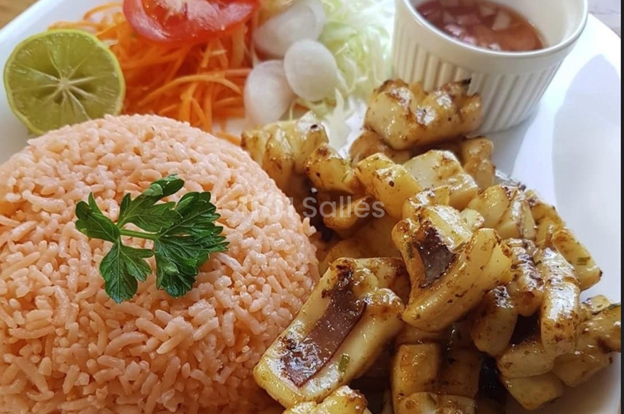 Assiette composée de riz orange, légumes frais, morceaux de calamars grillés et une sauce servie dans un ramequin.