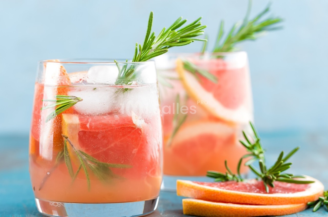 Deux verres de cocktail rose avec glaçons, tranches de pamplemousse et brins de romarin sur une table bleue.