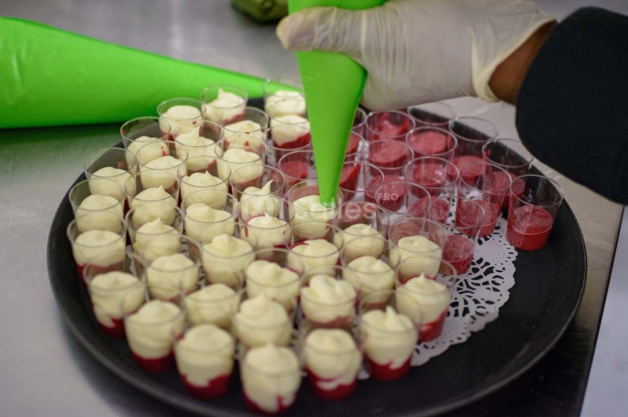 Préparation de verrines avec une poche à douille, contenant une mousse blanche sur un lit de coulis rouge.