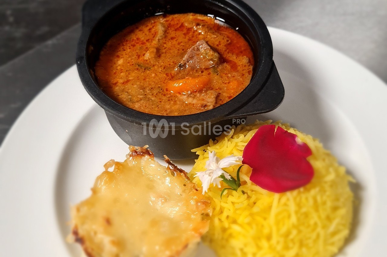 Plat composé d'un curry de viande en sauce, d'un gratin individuel et de riz jaune décoré de fleurs comestibles.