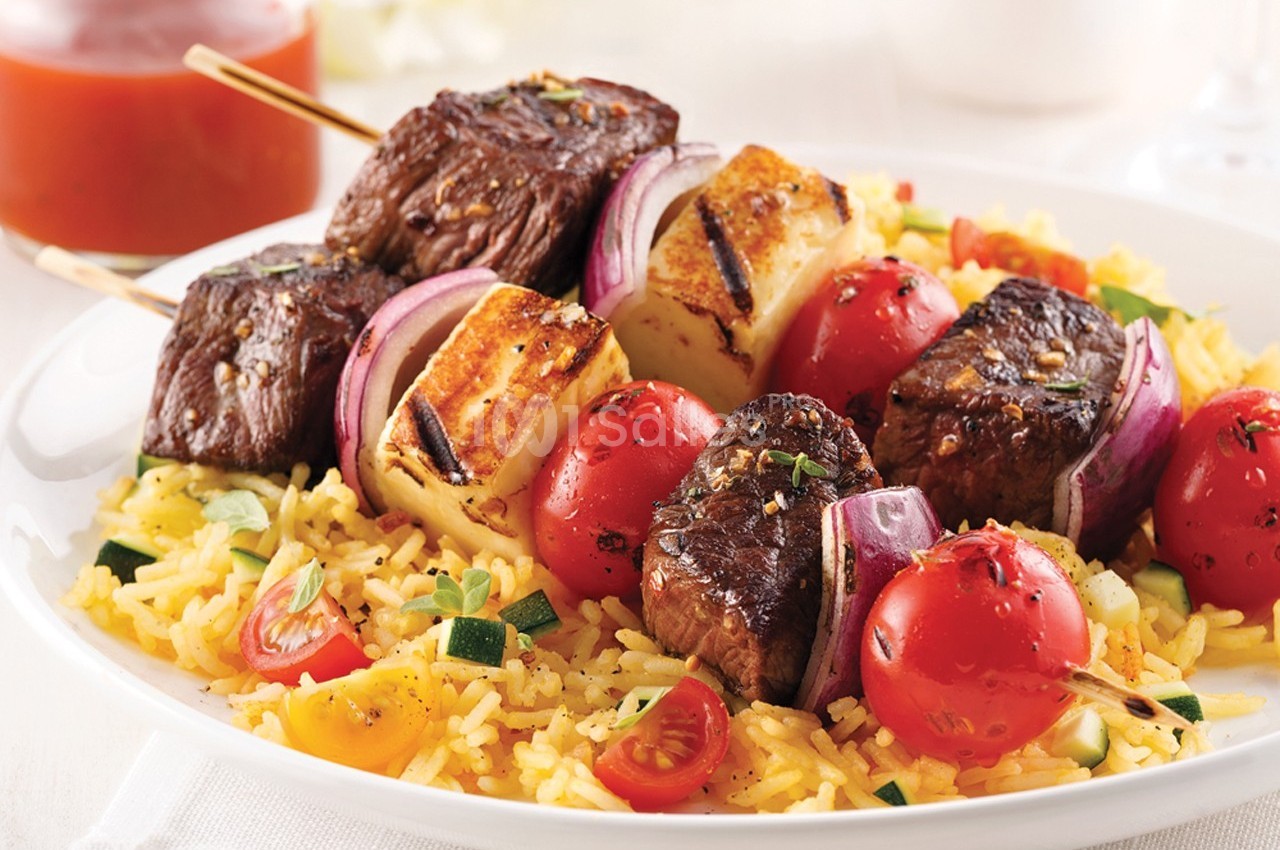 Brochettes de viande, fromage grillé, tomates et oignons sur un lit de riz aux légumes.