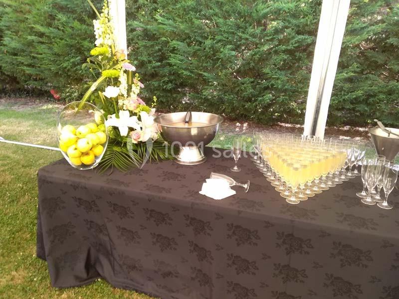 Table dressée avec nappes noires, verres alignés, vase de citrons, fleurs et bol métallique dans un jardin.