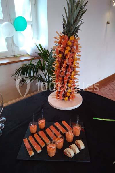 Ananas décoratif garni de brochettes de fruits, accompagné de verrines et bouchées sur une table de réception.