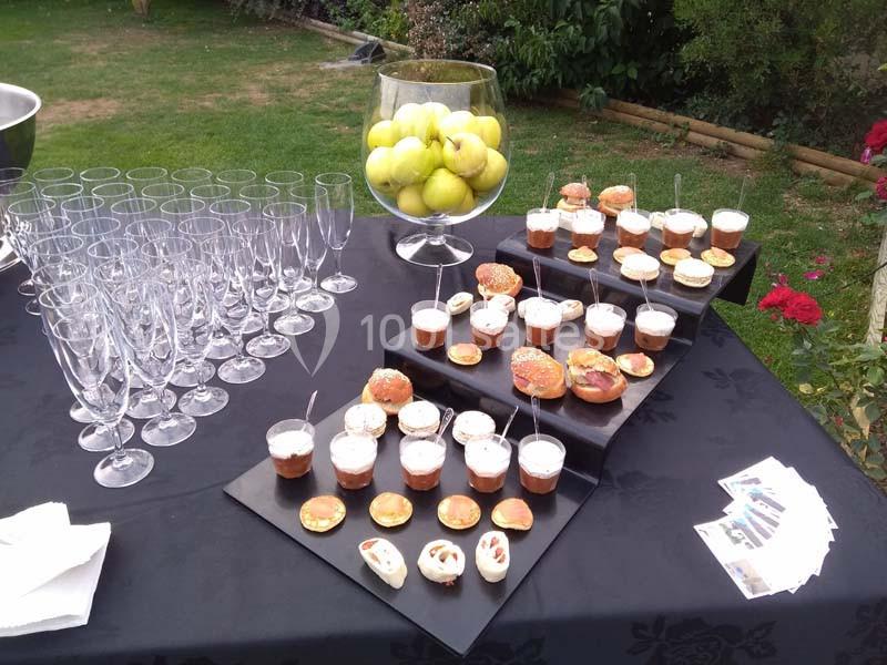 Table dressée avec des verrines, amuse-bouches, verres à champagne vides et une coupe remplie de pommes vertes.