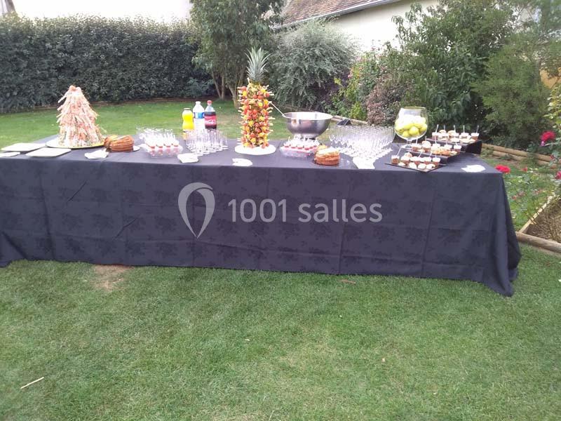 Table de buffet dressée en extérieur avec boissons, verrines, desserts et une pièce montée sur une nappe noire.