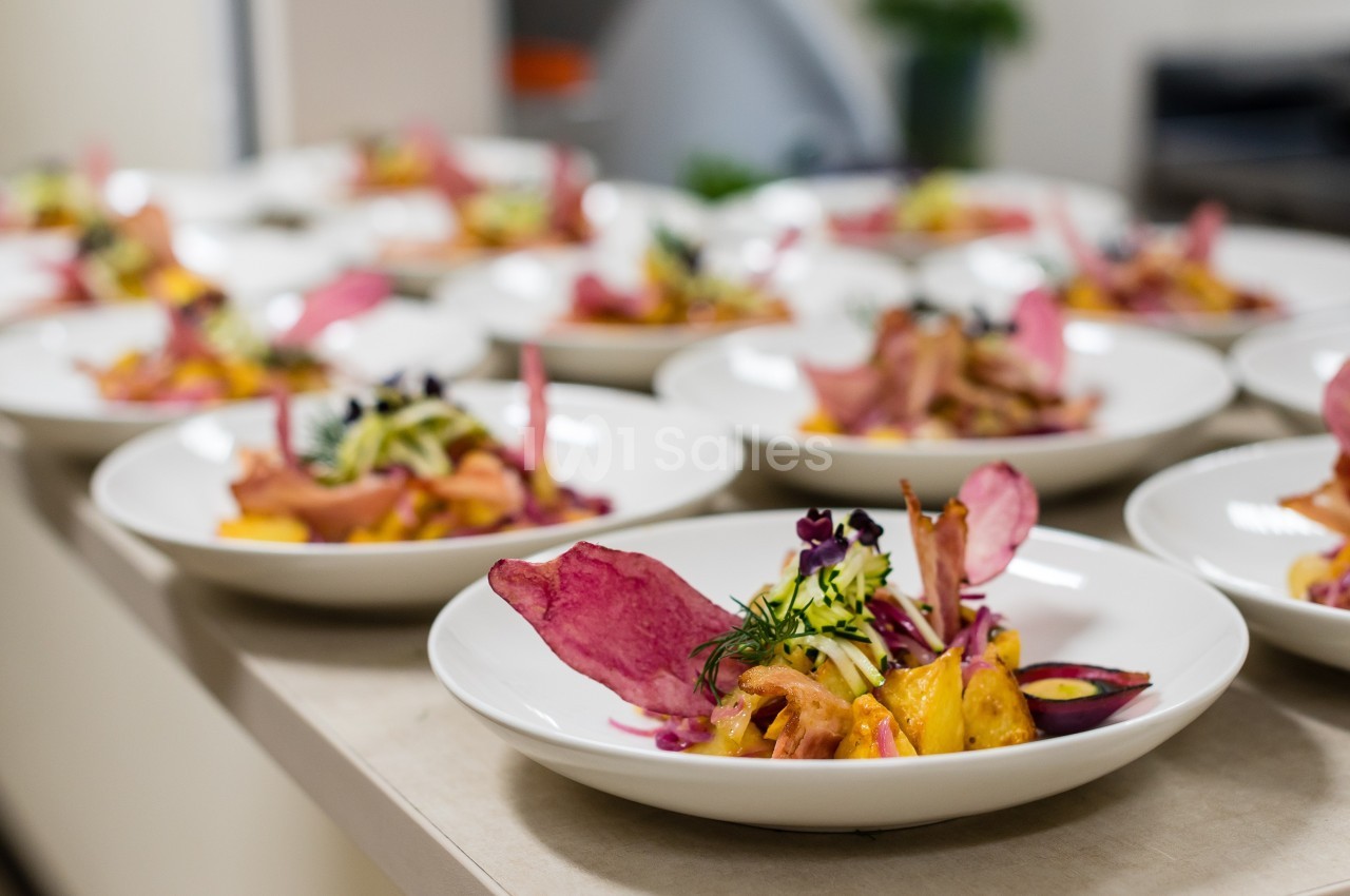 Assiettes de plats colorés avec légumes, chips de betterave et herbes fraîches alignées sur un plan de travail.