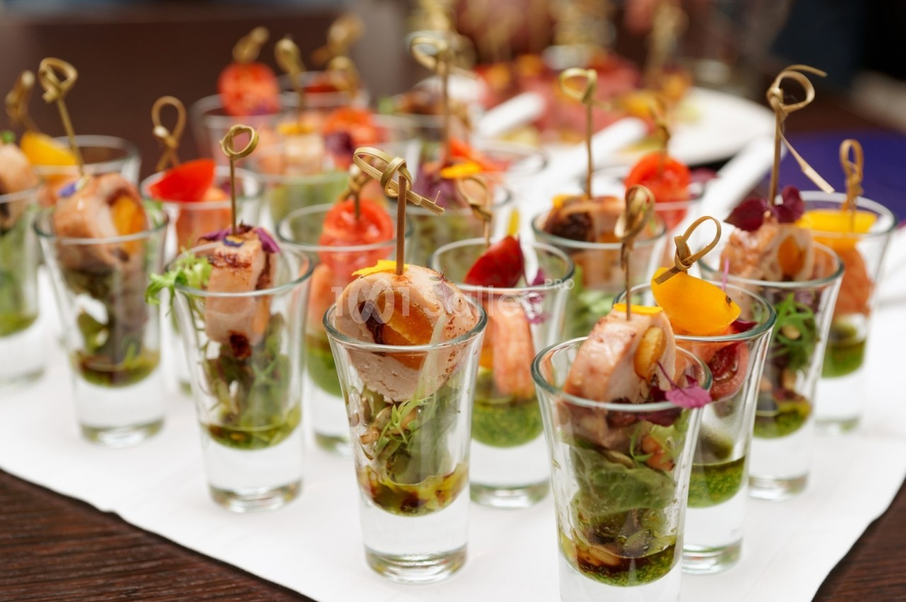 Verrines garnies de brochettes de viande et légumes colorés, présentées sur une table pour un buffet.