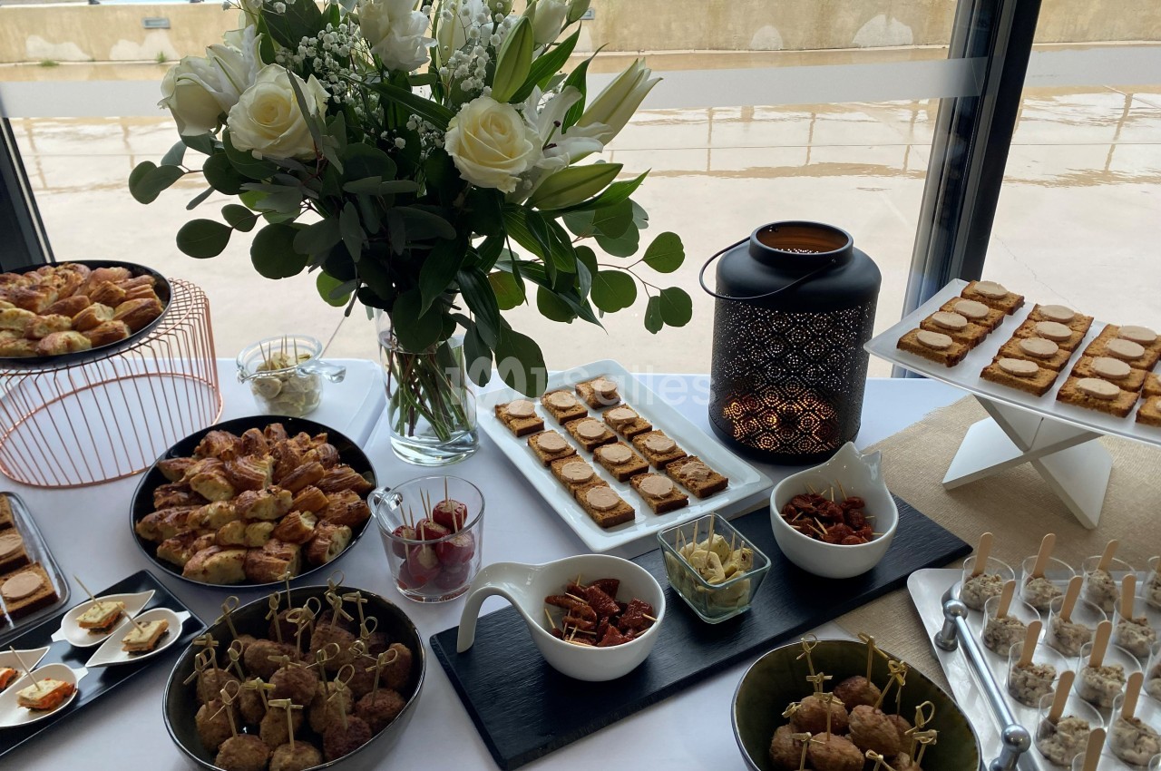 Buffet avec assortiment de bouchées salées, fleurs blanches en vase et lanterne décorative sur une table.