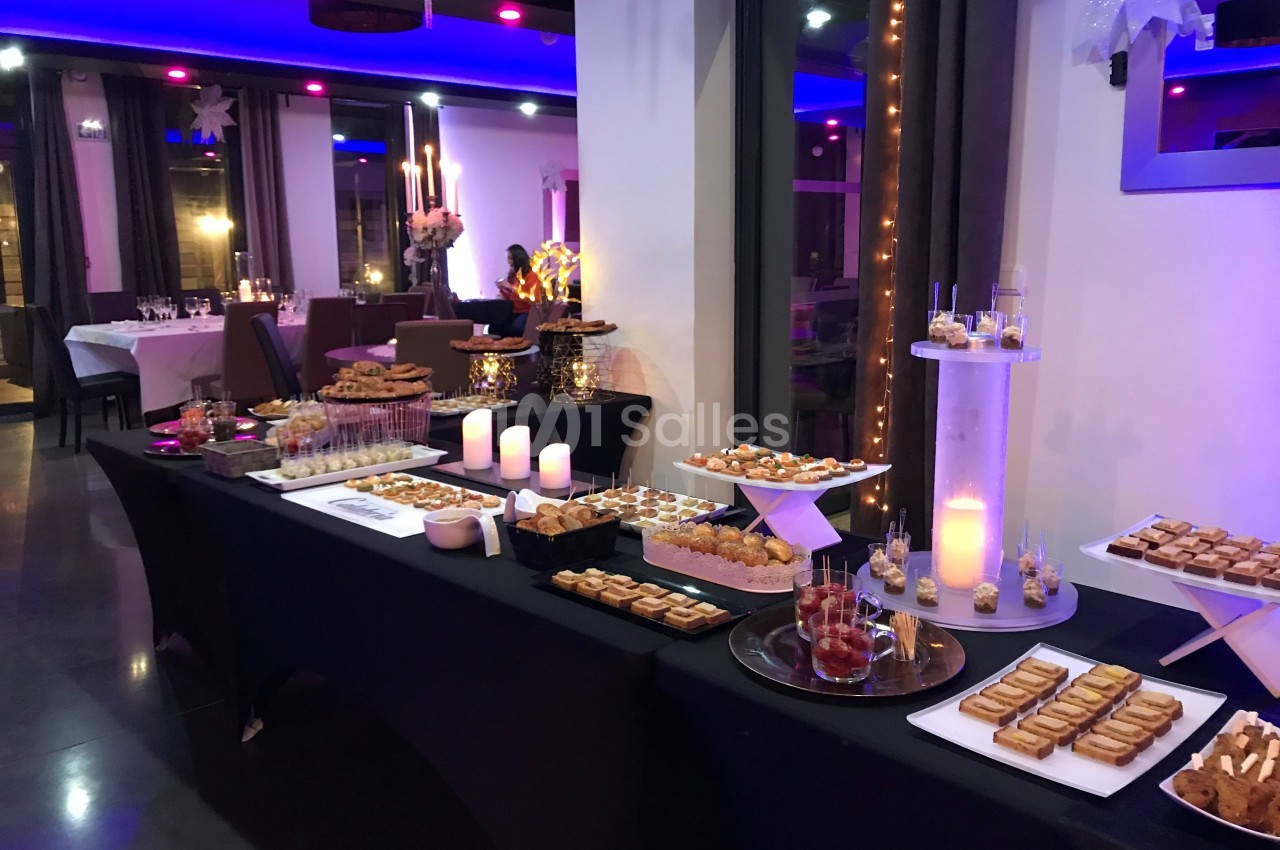 Buffet de desserts variés disposés sur des tables noires dans une salle éclairée par des lumières violettes et chaudes.