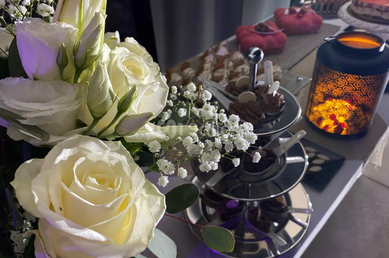 Bouquet de roses blanches et gypsophiles près d'un présentoir à desserts et d'une lanterne allumée.