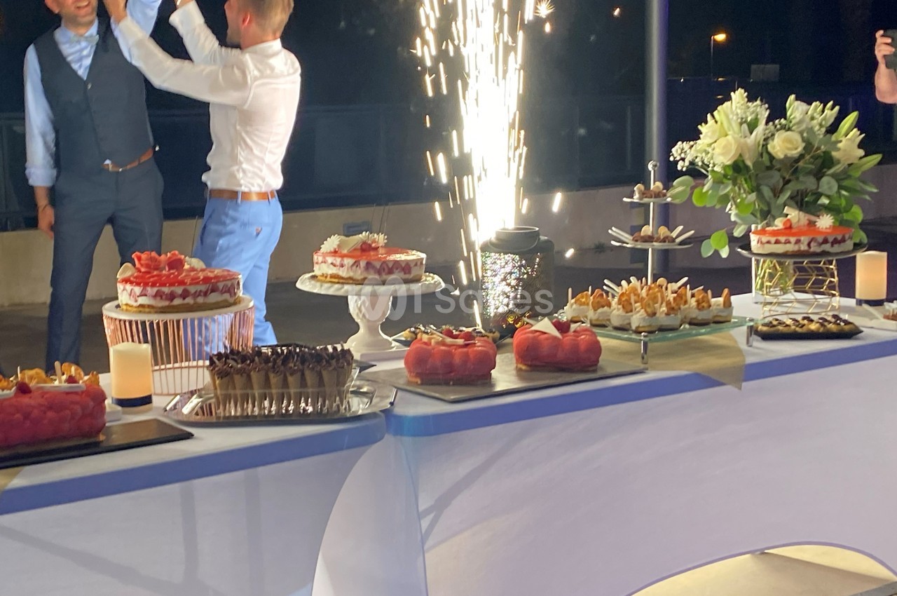 Table de desserts variés avec gâteaux, fleurs et fontaine lumineuse en arrière-plan lors d'une célébration nocturne.
