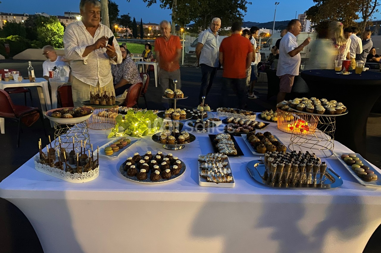 Table garnie de desserts variés lors d'un événement en soirée, avec des invités en arrière-plan.