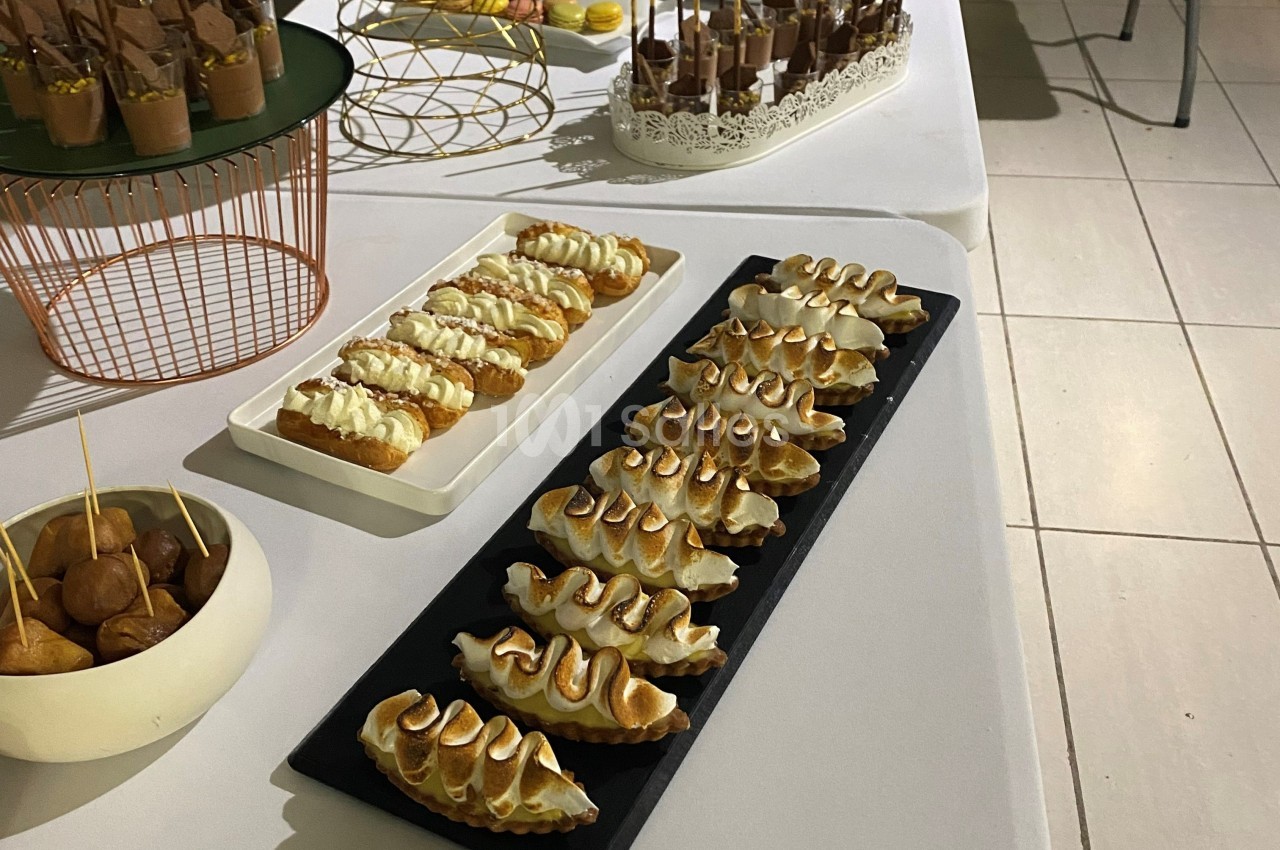 Plateau de pâtisseries variées, dont des éclairs et des desserts meringués, disposés sur une table blanche.