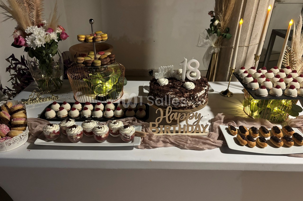 Table décorée pour un 18e anniversaire avec un gâteau au centre, cupcakes, macarons et autres pâtisseries.