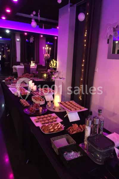 Buffet de réception avec divers plats et amuse-bouches disposés sur une table dans une salle éclairée par des lumières…