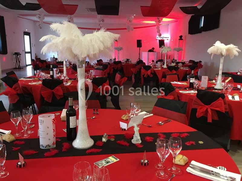 Salle décorée pour un événement avec des tables rouges et noires, centres de table à plumes blanches et ambiance lumineuse…