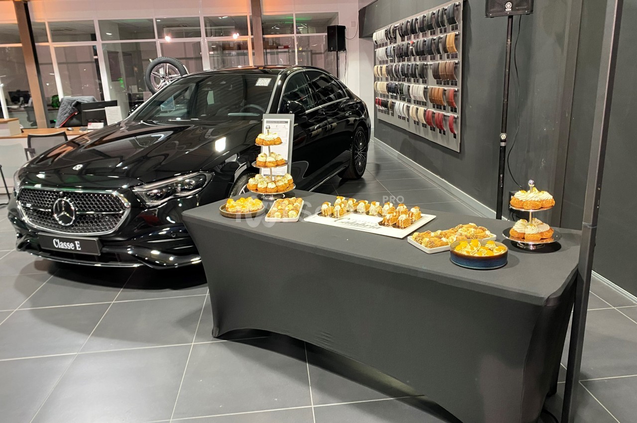 Voiture noire exposée dans un showroom à côté d'une table garnie de pâtisseries sur un nappage noir.