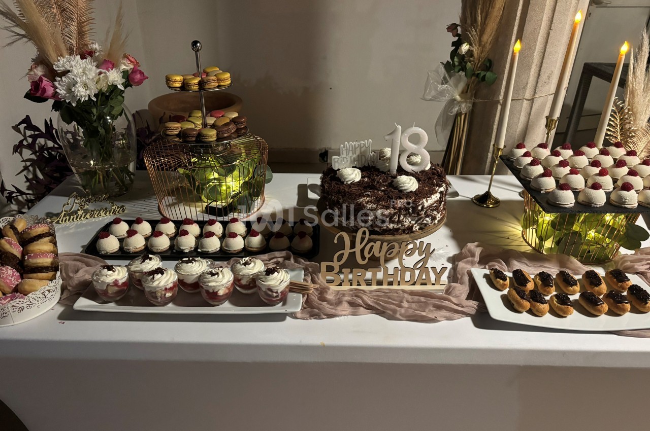 Table décorée avec des desserts variés, gâteau d'anniversaire ’18 ans’ au centre, bougies et fleurs en arrière-plan.