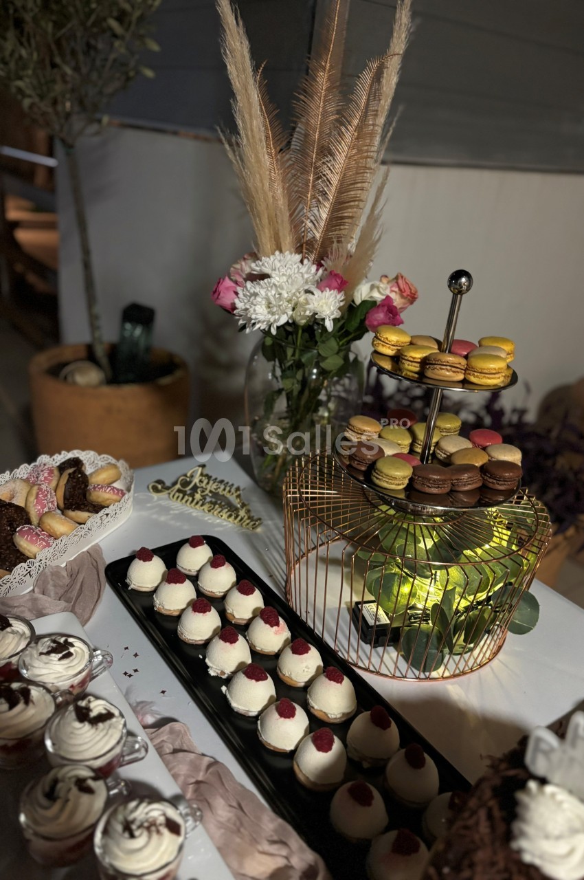 Plateau de desserts variés comprenant macarons, verrines, pâtisseries et fleurs en décoration sur une table.