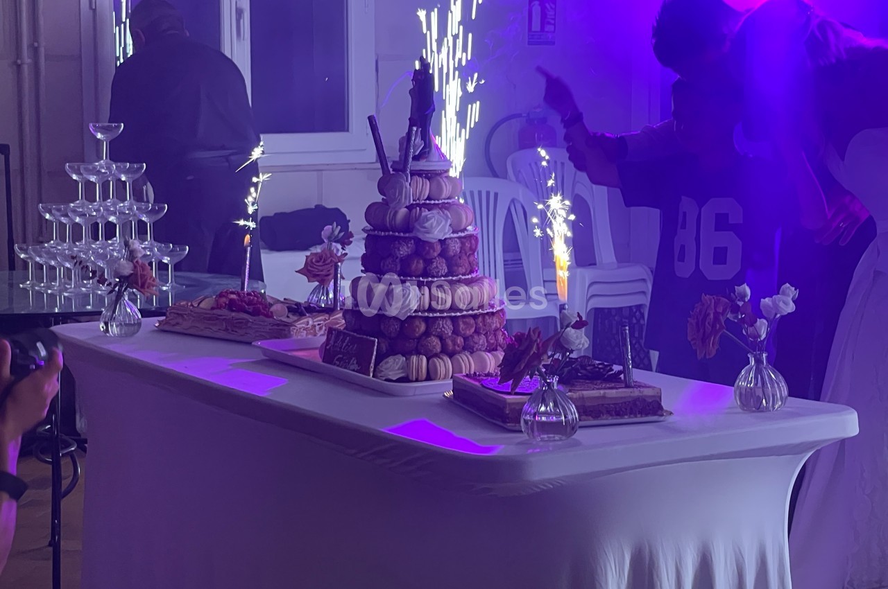 Table de fête décorée avec une pièce montée de choux, des desserts, des fleurs et des fontaines lumineuses allumées.