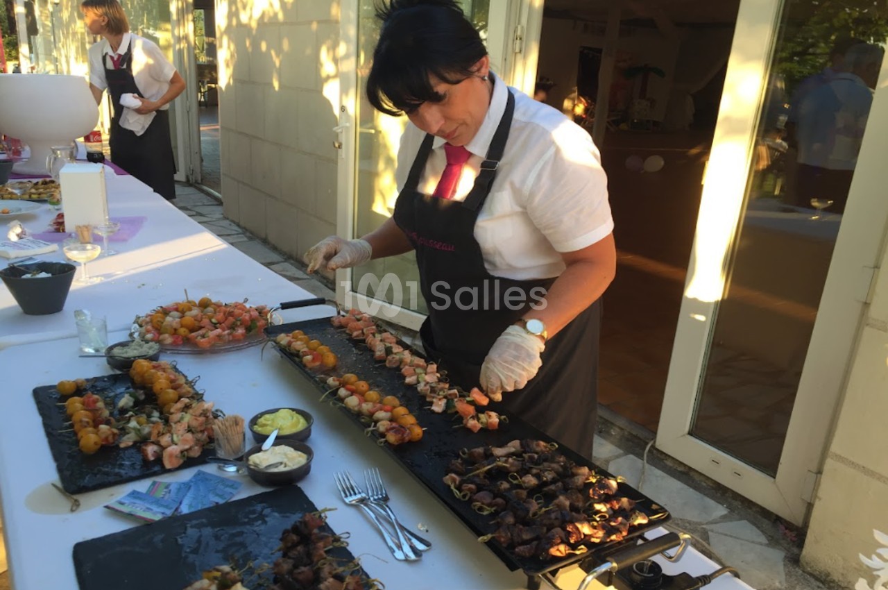 Une femme en tablier prépare des brochettes sur des plateaux lors d'un buffet en extérieur.