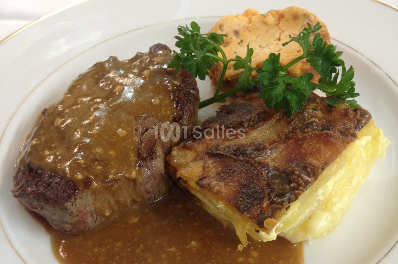 Assiette contenant un filet de viande avec sauce, gratin de pommes de terre, galette et garniture de persil.