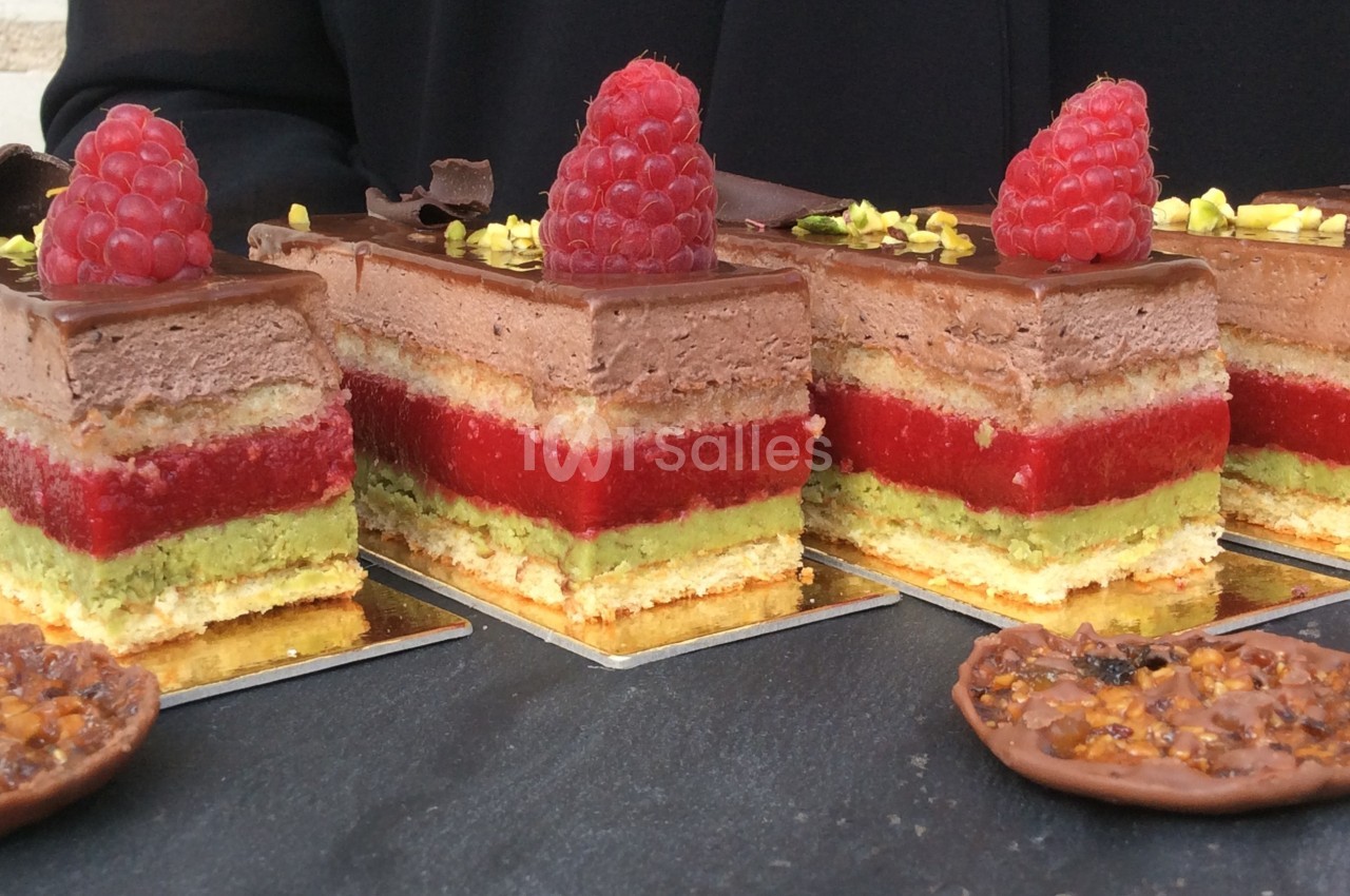 Gâteaux à étages avec mousse au chocolat, gelée rouge, crème verte, décorés de framboises et éclats de pistache.