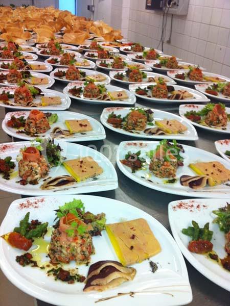 Assiettes dressées avec foie gras, tartare de poisson, légumes et garnitures, alignées sur un plan de travail en cuisine.