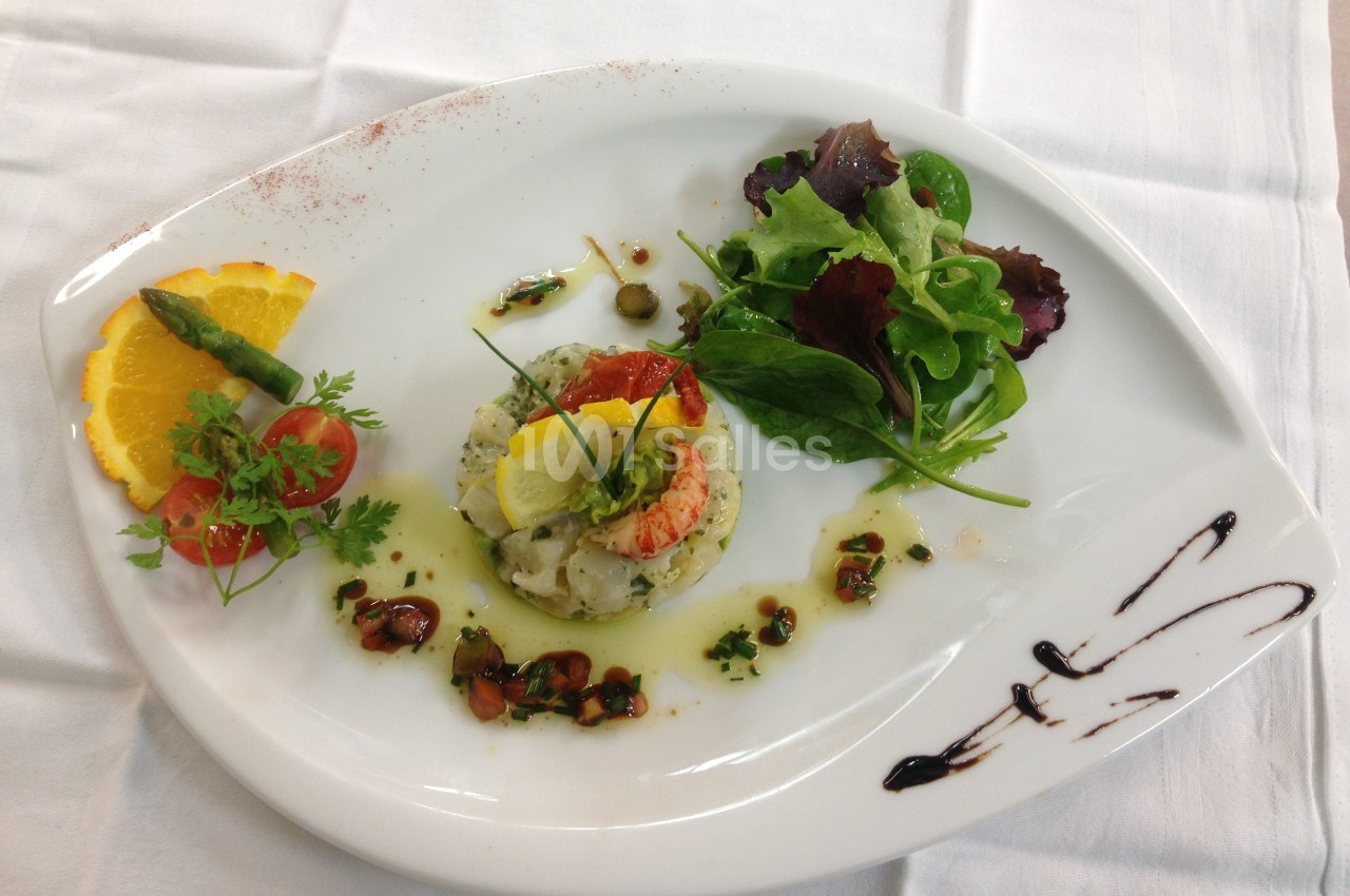 Assiette gastronomique avec tartare de poisson, salade verte, asperge, tranche d'orange et décoration de sauce balsamique.