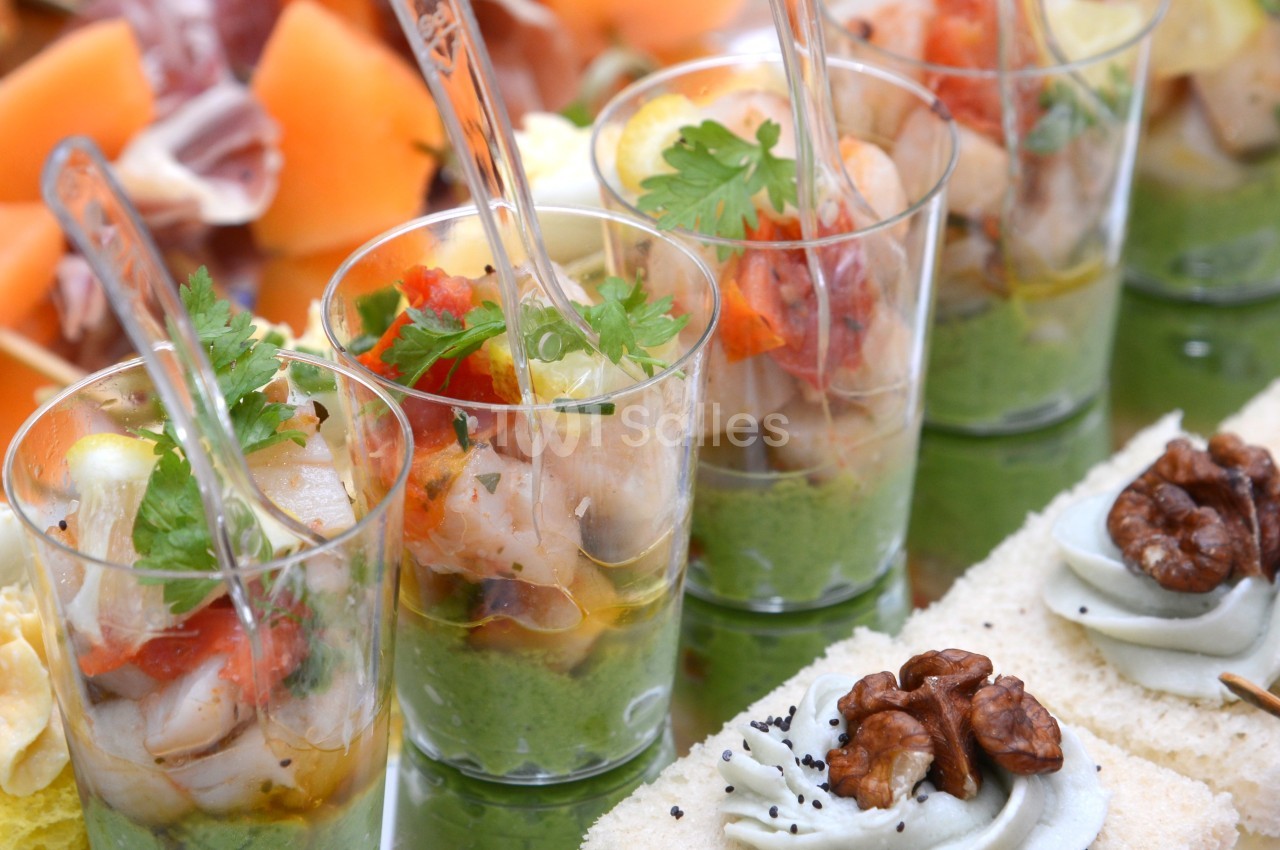 Assortiment de verrines et amuse-bouches colorés avec fruits, noix, crevettes et herbes fraîches.