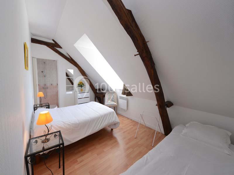 Chambre mansardée avec deux lits simples, parquet clair, poutres apparentes et lumière naturelle provenant d'un velux.