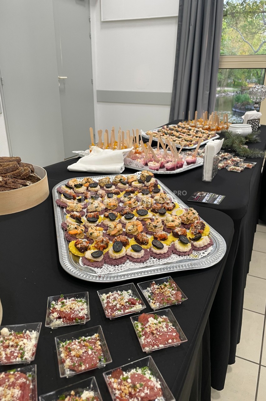 Plateau de canapés variés et verrines disposés sur une table noire lors d'un buffet en intérieur.