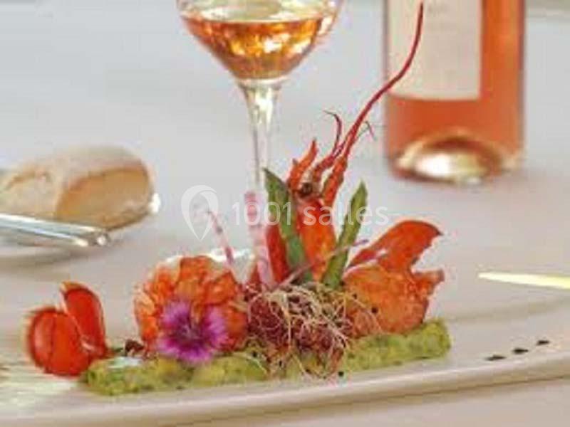 Assiette gastronomique avec langoustines, purée verte, fleurs comestibles et germes, accompagnée d'un verre de vin rosé.