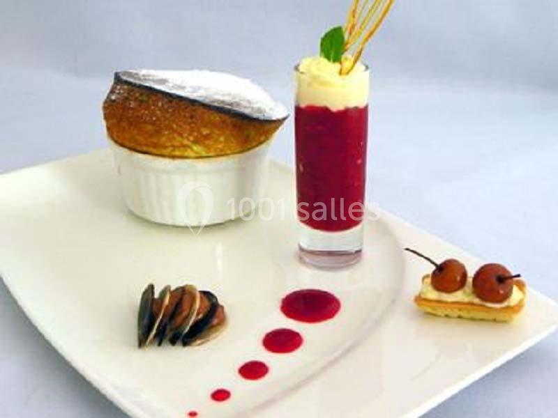 Dessert gastronomique composé d'un soufflé, d'un verre de coulis rouge, de fruits et d'une petite pâtisserie.