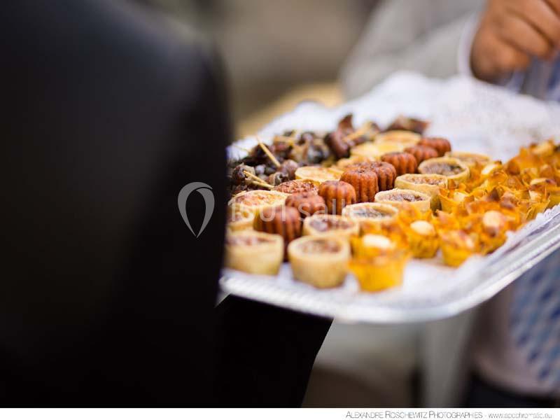 Plateau de petits desserts variés, incluant tartelettes, cannelés et autres pâtisseries, tenu par une personne.